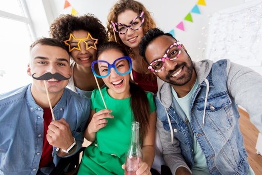 Partyteilnehmer mit Brillen- und Schnurrbartrequisiten aus Pappe nehmen ein Selfie auf.